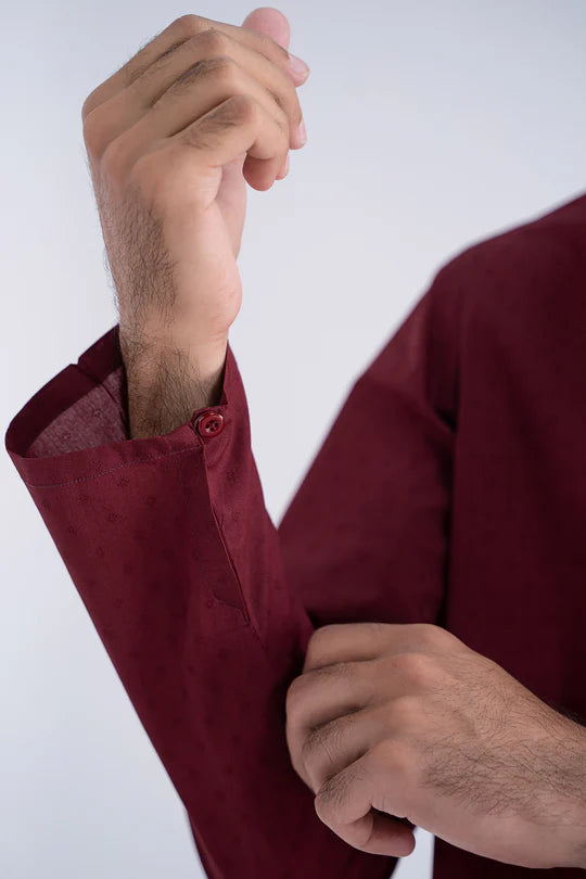 Close-up of a person wearing a burgundy shirt with rolled-up sleeves against a white background