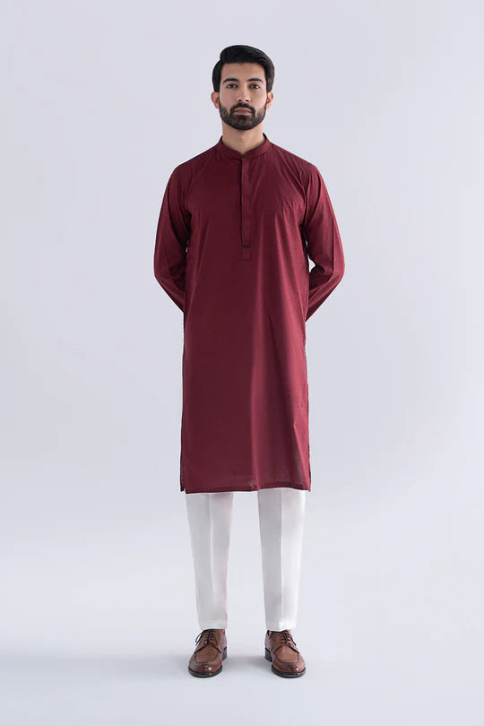 Man wearing a maroon kurta with white pants on a light gray background