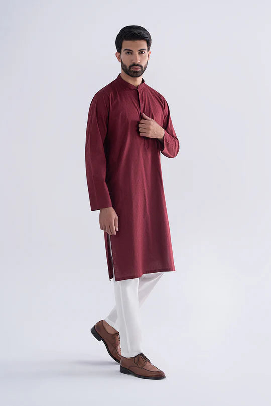 Man wearing a maroon kurta with white pants on a light gray background