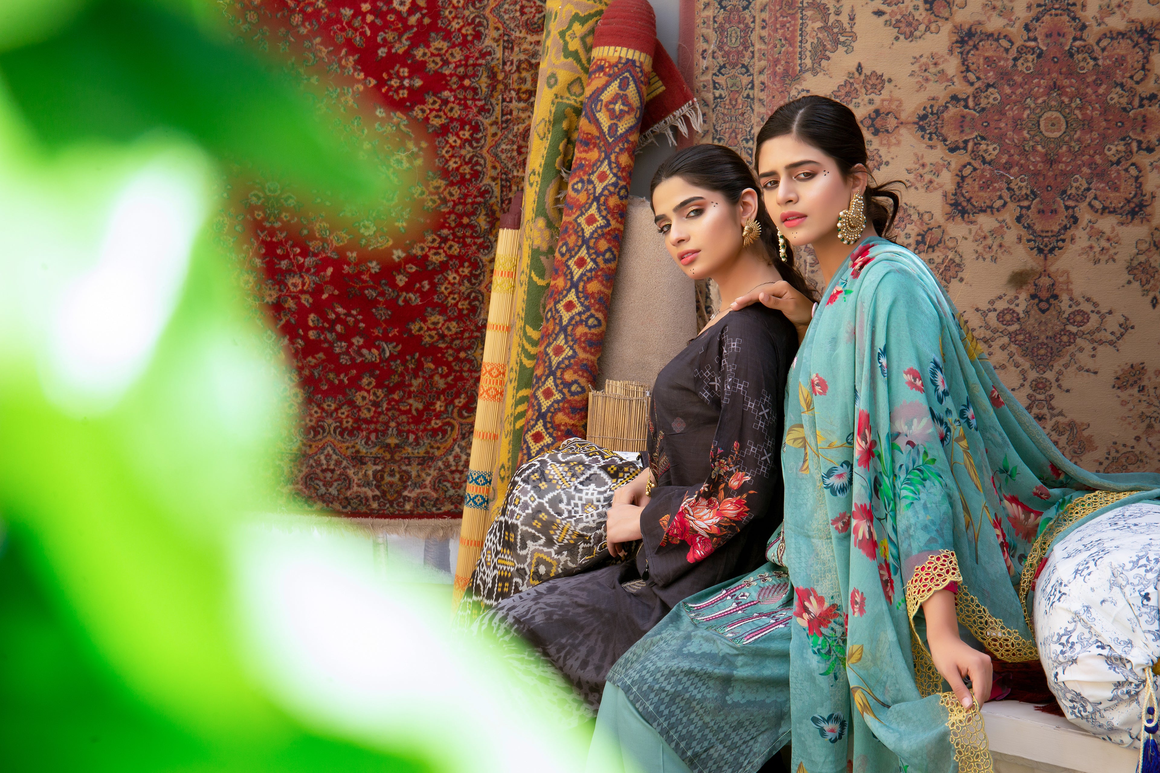 Two women in traditional attire sitting in a room with patterned walls and furniture.