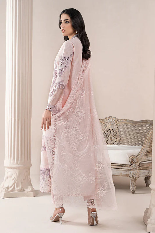 Woman in a light pink embroidered outfit standing in an elegant room with a decorative chair.
