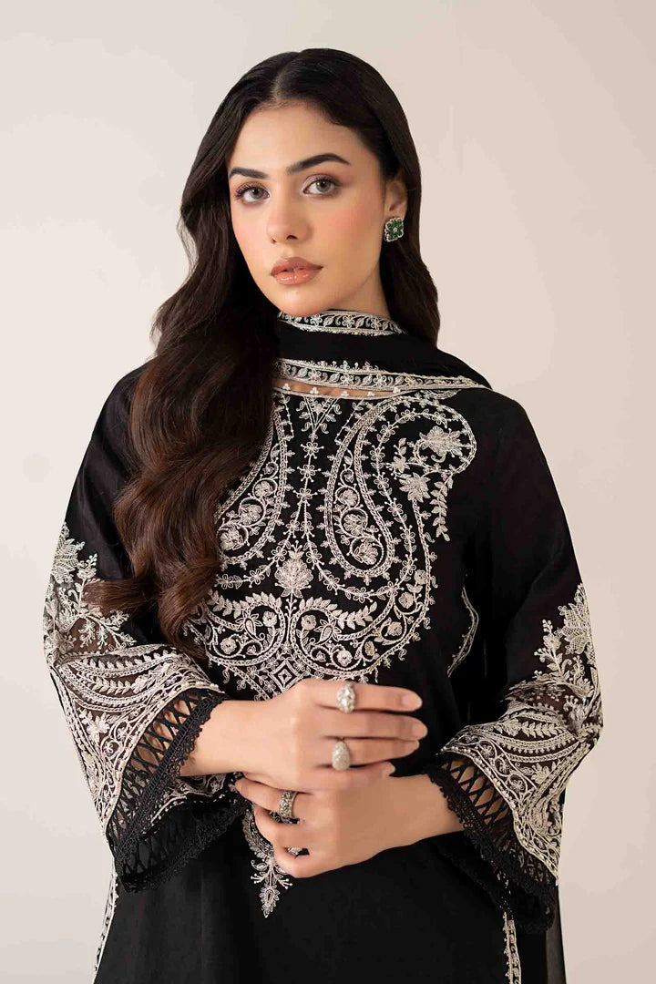 Woman wearing a black outfit with intricate white embroidery on a plain background