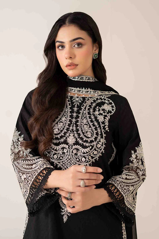 Woman wearing a black outfit with intricate white embroidery on a plain background