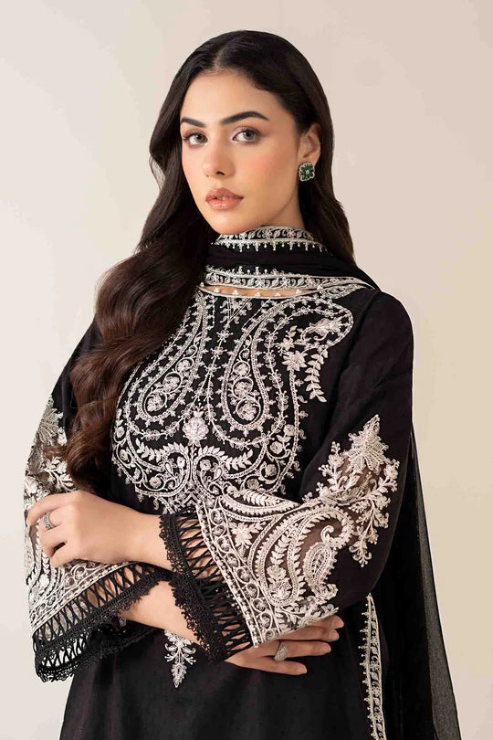 Woman wearing a black outfit with intricate white embroidery on a plain background
