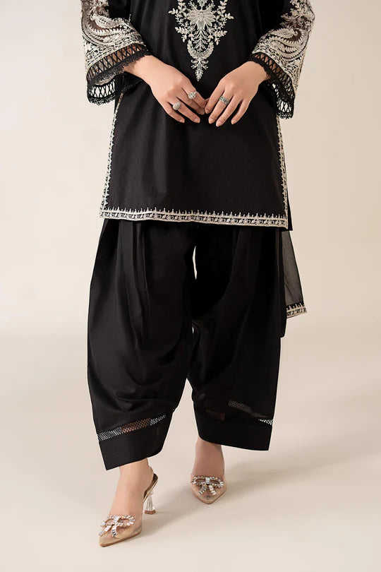 Person wearing a black traditional outfit with intricate embroidery on a beige background