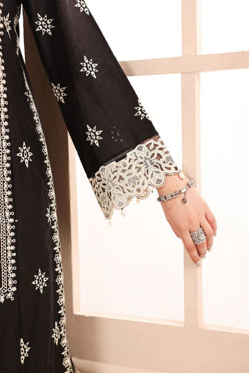 Black embroidered garment with white patterns, worn by a person, against a neutral background.