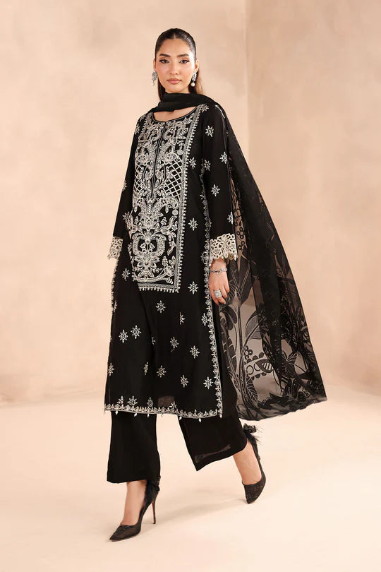 Woman wearing a black embroidered outfit with a sheer dupatta on a beige background