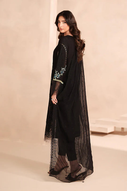 Woman wearing a black outfit with sheer overlay against a beige background
