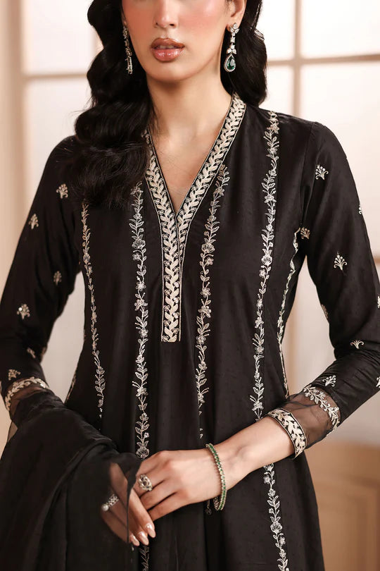 Woman wearing a black dress with intricate white embroidery against a neutral background