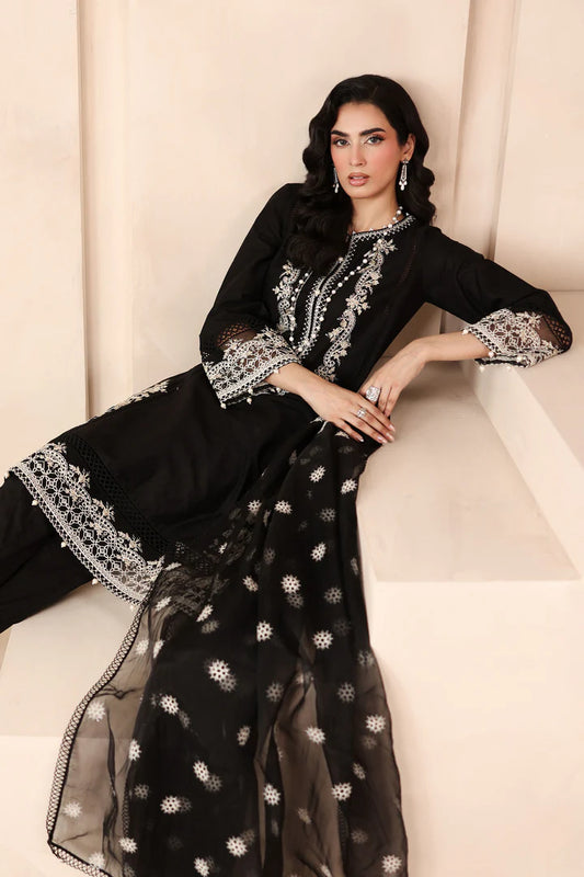 Woman wearing a black and white embroidered traditional outfit sitting on a white couch.