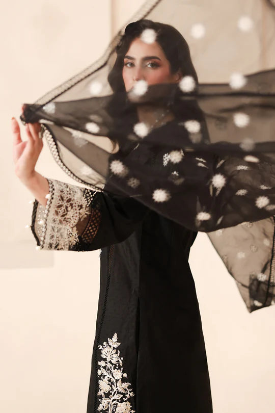 Woman wearing a black abaya with white embroidery, holding a sheer black scarf.