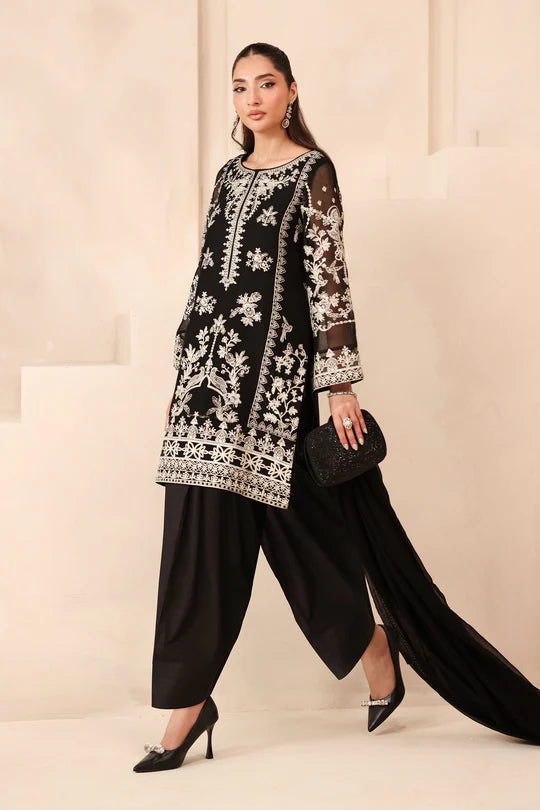 Woman wearing a black and white embroidered outfit with black pants against a beige background