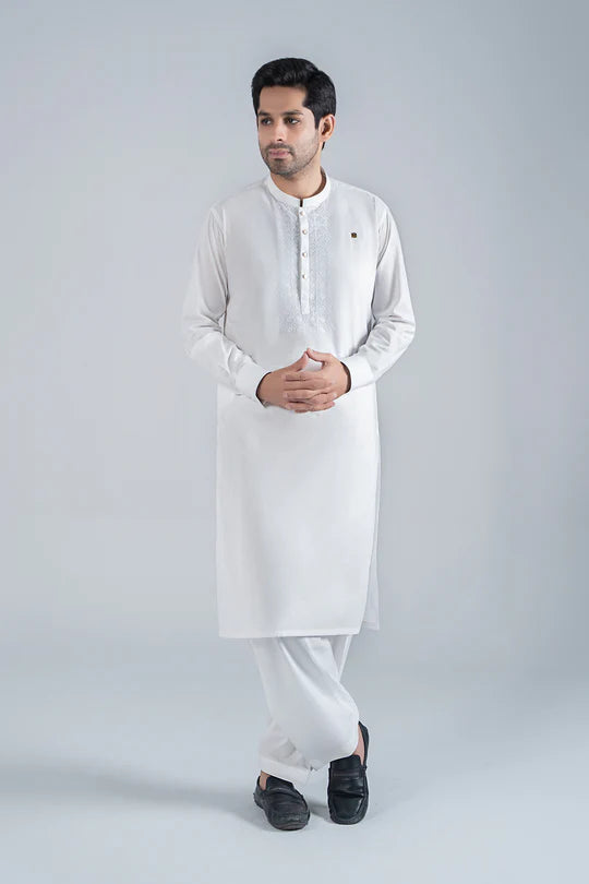 Man wearing a white kurta with black shoes on a light gray background