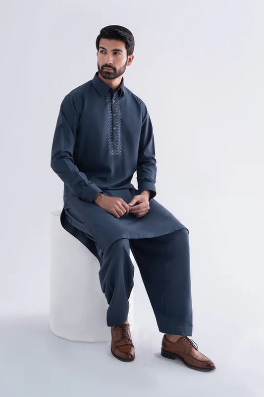 Man wearing a traditional outfit sitting on a white stool against a light gray background