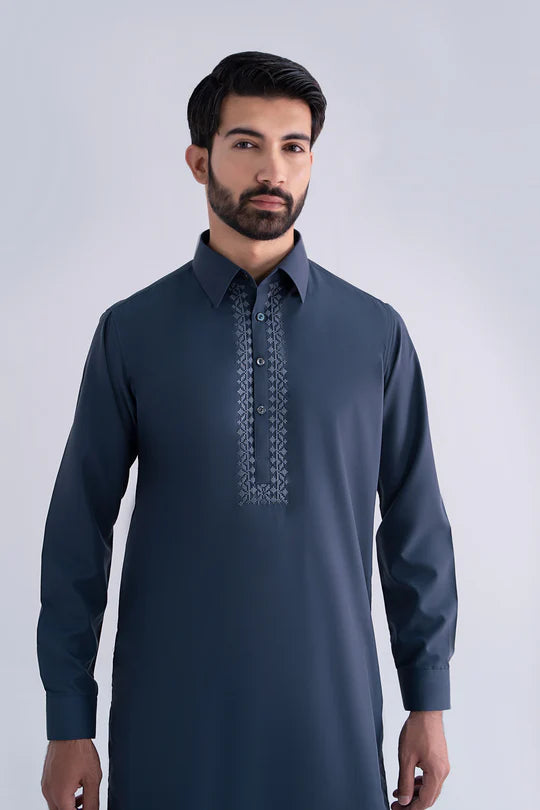 Man wearing a dark blue embroidered shirt against a light gray background