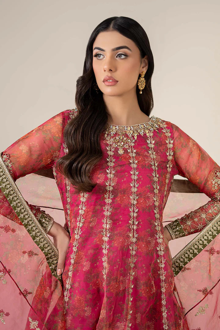 Woman wearing a pink and red embroidered traditional outfit with gold jewelry against a neutral background