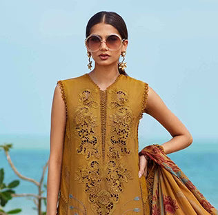 Woman wearing a mustard yellow embroidered outfit with sunglasses and a scarf against a clear blue sky.